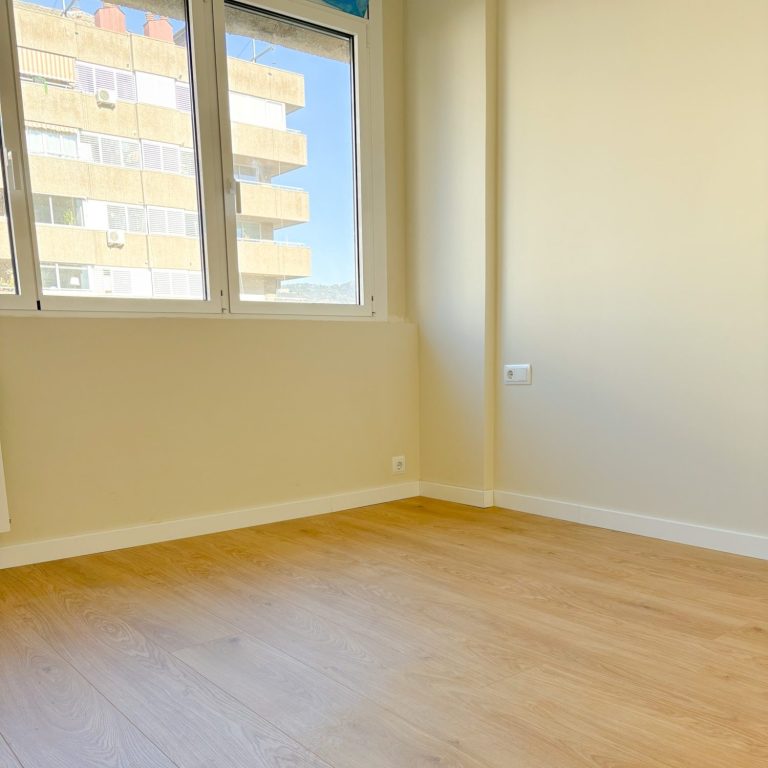 Pintura Habitación vacía con paredes pintadas beige y suelo de madera, ventana con acceso a balcón.