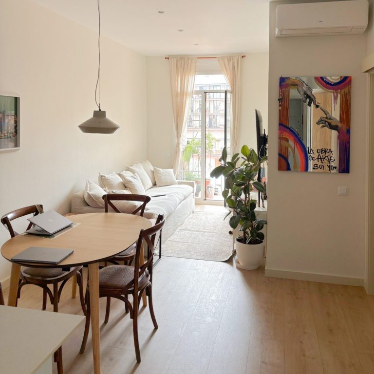 Reformas Integrales Salón moderno con sofá claro, mesa de madera y televisión en pared. Luminoso y acogedor.